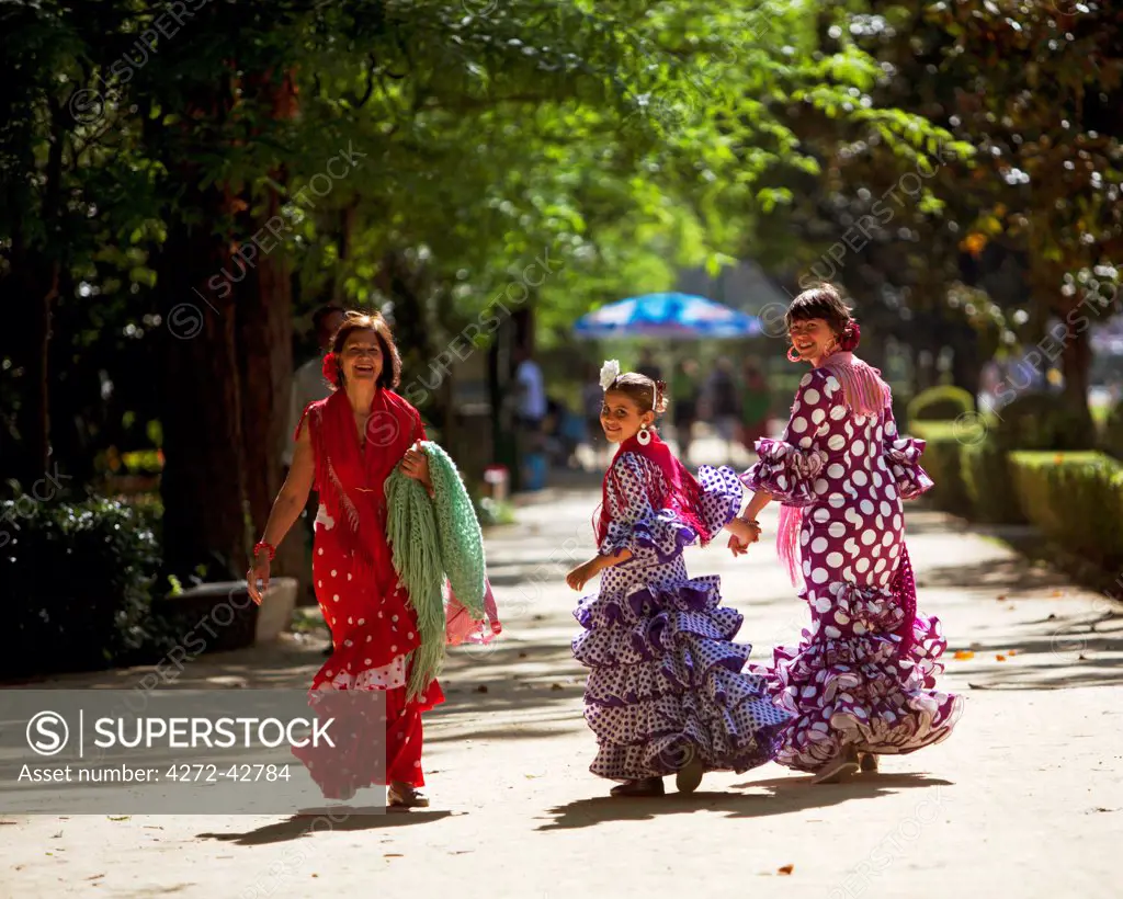Seville, Andalusia, Spain, Two women and a girl in traditional flamenco dresses walking during the Feria de Abril