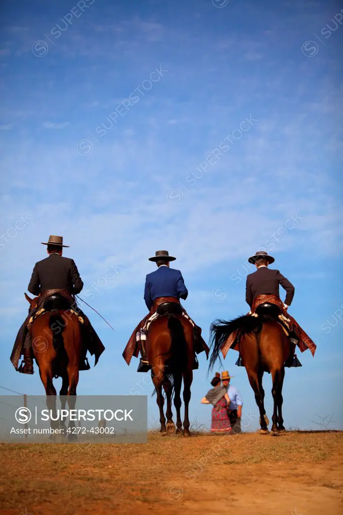 Seville, Andalusia, Spain. Three men in cowboy clothes horseriding to the village of El Rocio with a couple in the background