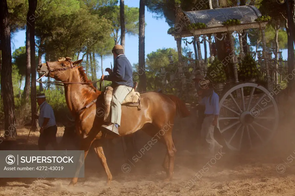 Huelva, Southern Spain. A Pilgrim on horseback with the float of the Madonna in the background on the way to the village of El Rocio for the annual Romeria