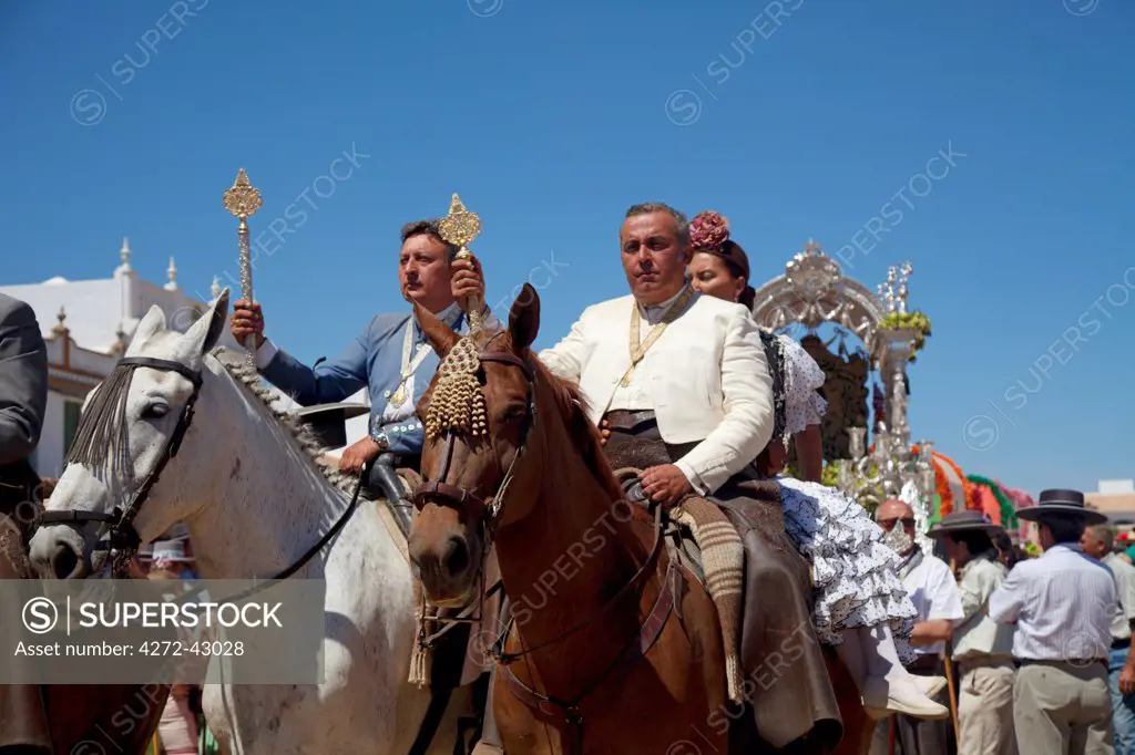 El Rocio, Huelva, Southern Spain. Man with woman companions in traditional clothes horseriding towards the church in the village of El Rocio during the annual Romeria