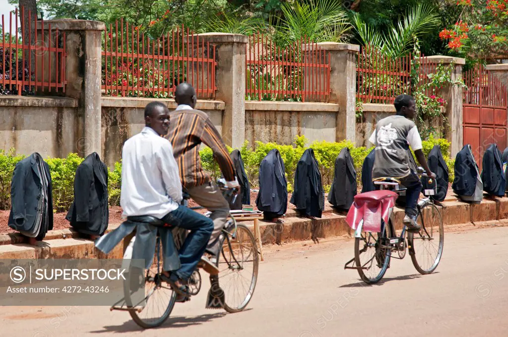 Bicycle taxis, known as Bodaboda, pass a novel display of new and second hand jackets, which are for sale on roadside posts in Lira town, Uganda, Africa