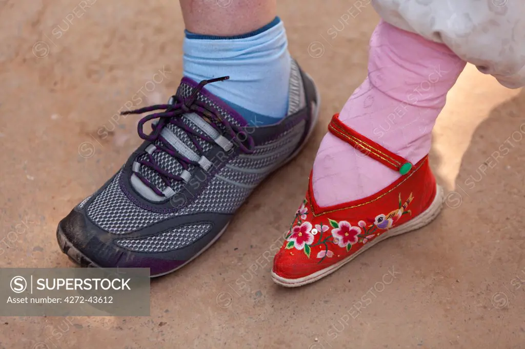 China, Yunnan, Liuyi. A tiny bound foot compared in size to a tourist's shoe, in the village of Liuyi.