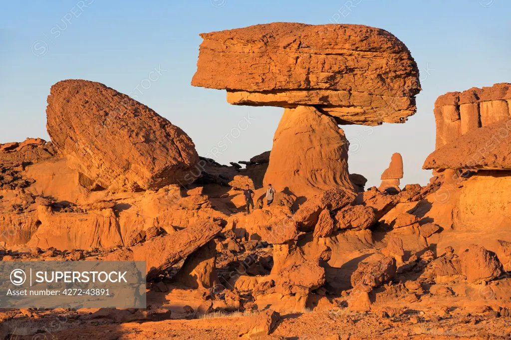 Chad, Chigeou, Ennedi, Sahara. A ridge of weathered red sandstone with two visitors giving scale to the giant mushroom like feature.
