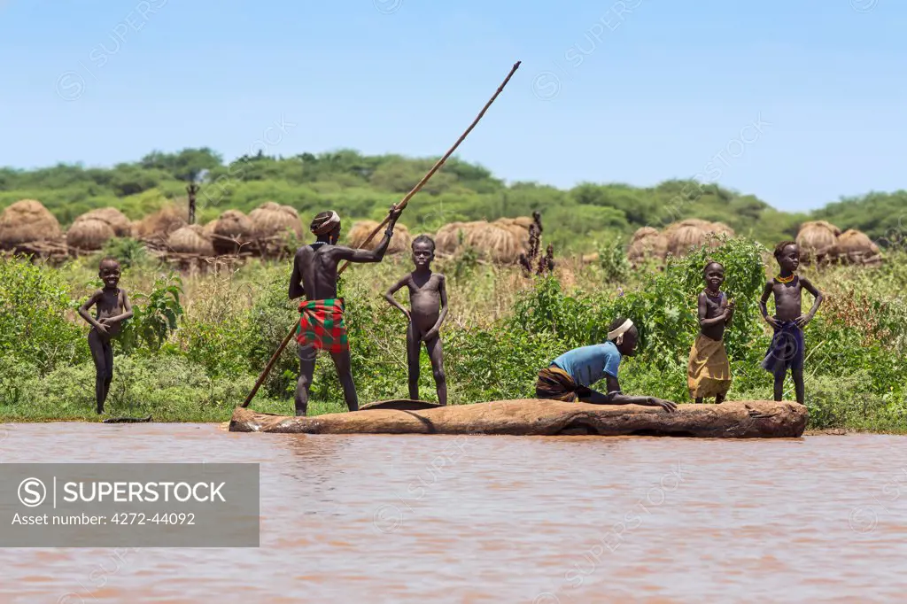 A man poles a dugout canoe past a Dassanech village near the banks of the Omo River, Ethiopia