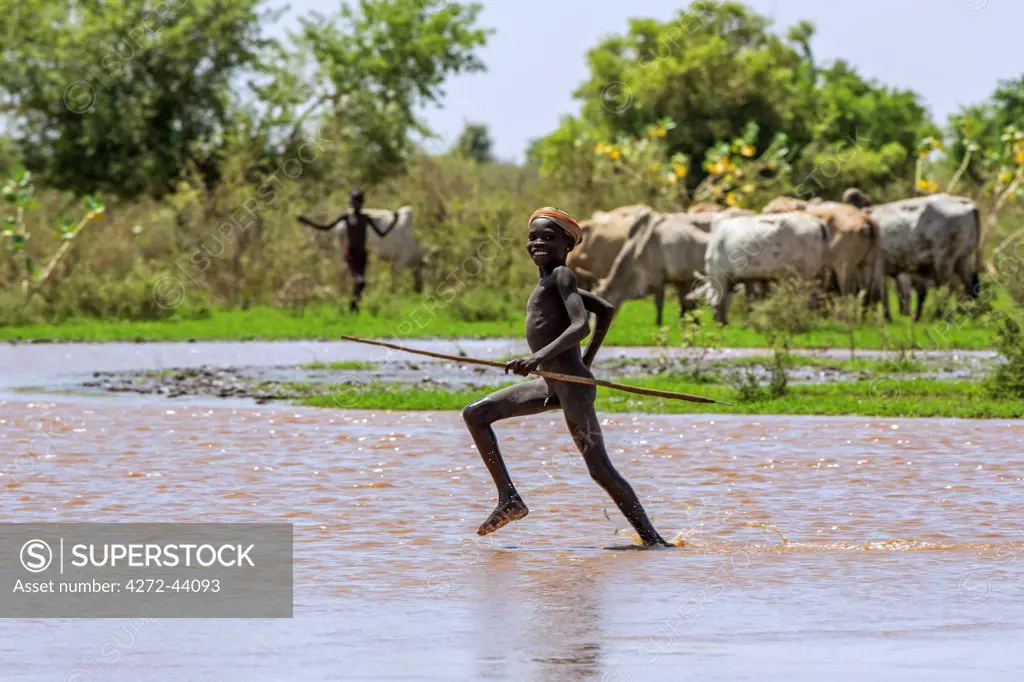 A young Dassanech herdsboy runs across shallow water beside the Omo River. The river bursts its banks annually during heavy rain in the Ethiopian Highlands, Ethiopia