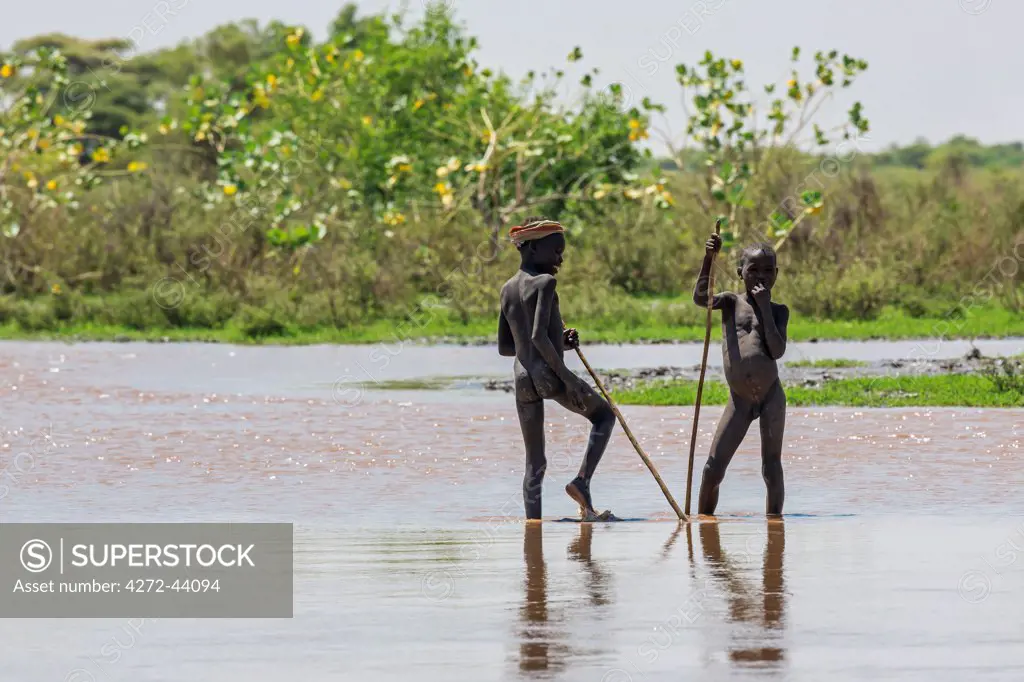 Two young Dassanech herdsboys pause in shallow water beside the Omo River. The river bursts its banks annually during heavy rain in the Ethiopian Highlands, Ethiopia
