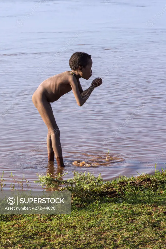 A young Dassanech boy drinks muddy water from the Omo River, Ethiopia