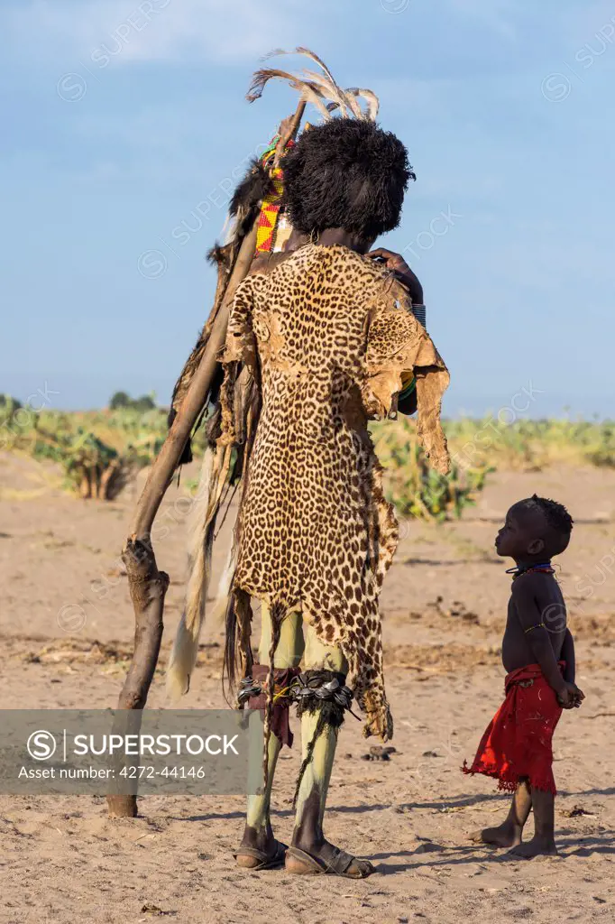 Watched by his daughter, a Dassanech man dresses in Dimi regalia, Ethiopia
