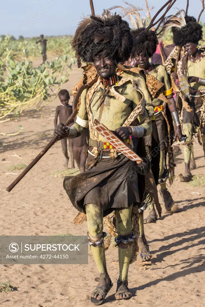 Dassanech men dressed in ceremonial Dimi regalia march in single file to dance, Ethiopia