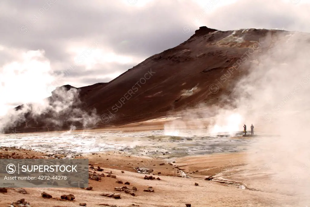 Tourists viewing the boiling mud pits, fumaroles and sulphur stained deposits at Hverarond beneath Namafjall mountain, near Lake Myvatn in northern Iceland