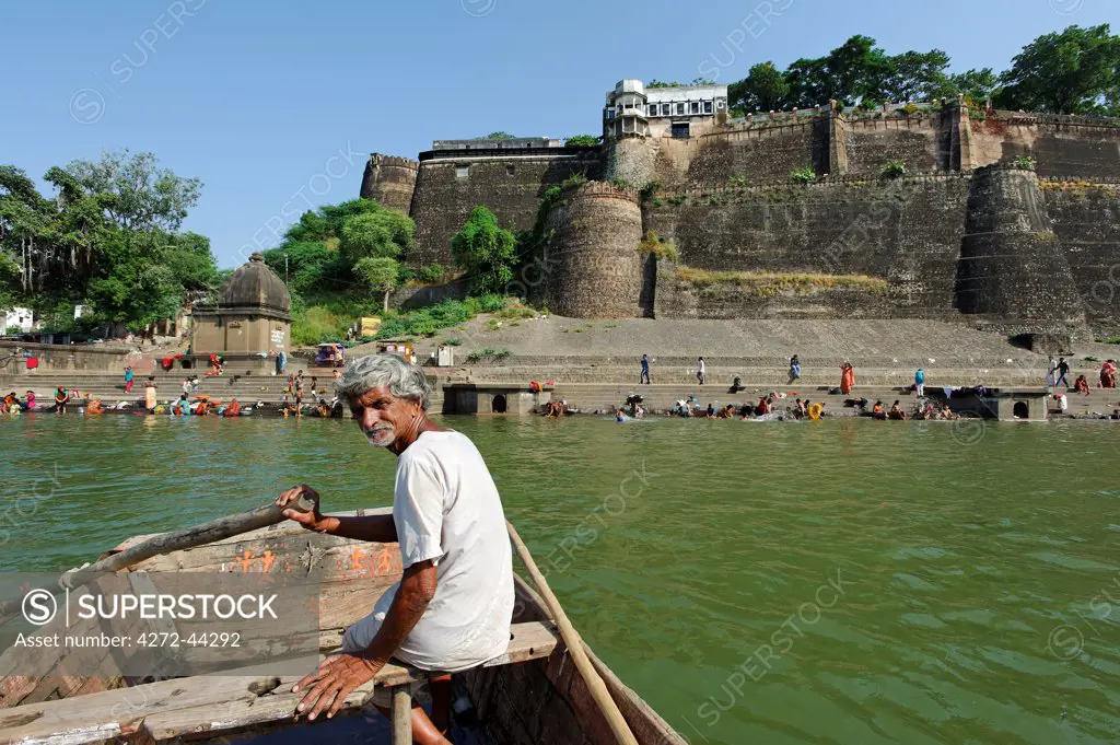 India, Madhya Pradesh, Maheshwar. Below Ahilya Fort, home to the royal Holkar dynasty and now a small luxury hotel, a boatman approaches bathing ghats on the Narmada River.