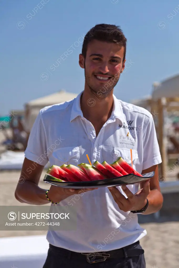 Italy, Forte dei Marmi. A handsome waiter carrying fresh watermelon at Twiga, a luxury beach club owned by Flavio Briatore.