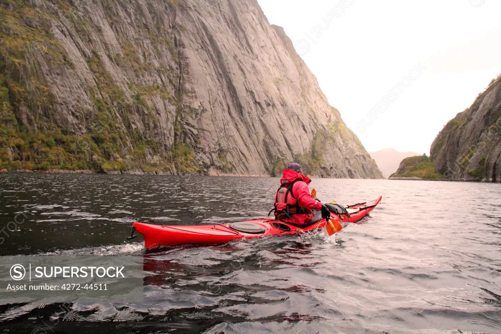 Sea kayaker paddling beneath sheer cliffs in Trollfjord, a 2km long inlet of the Raftsund between the Lofoten and Vesteralen Islands, Norway