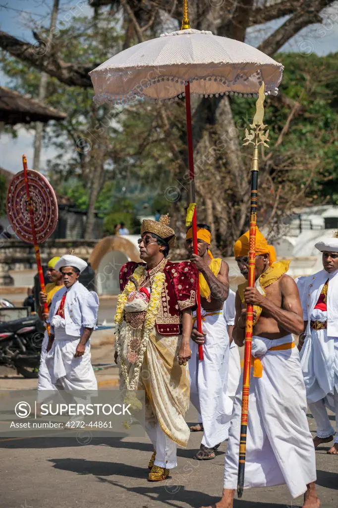 A high official of the Temple of the Sacred Tooth Relic dressed in traditional regalia and attended by lance, sunshade and umbrella bearers participates in the Kandy Day Perahera, Sri Lanka