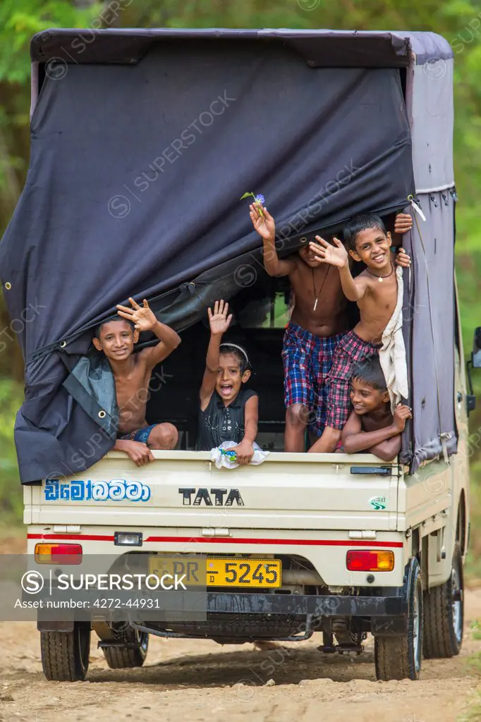 Happy children wave from the back of a moving truck, Sri Lanka