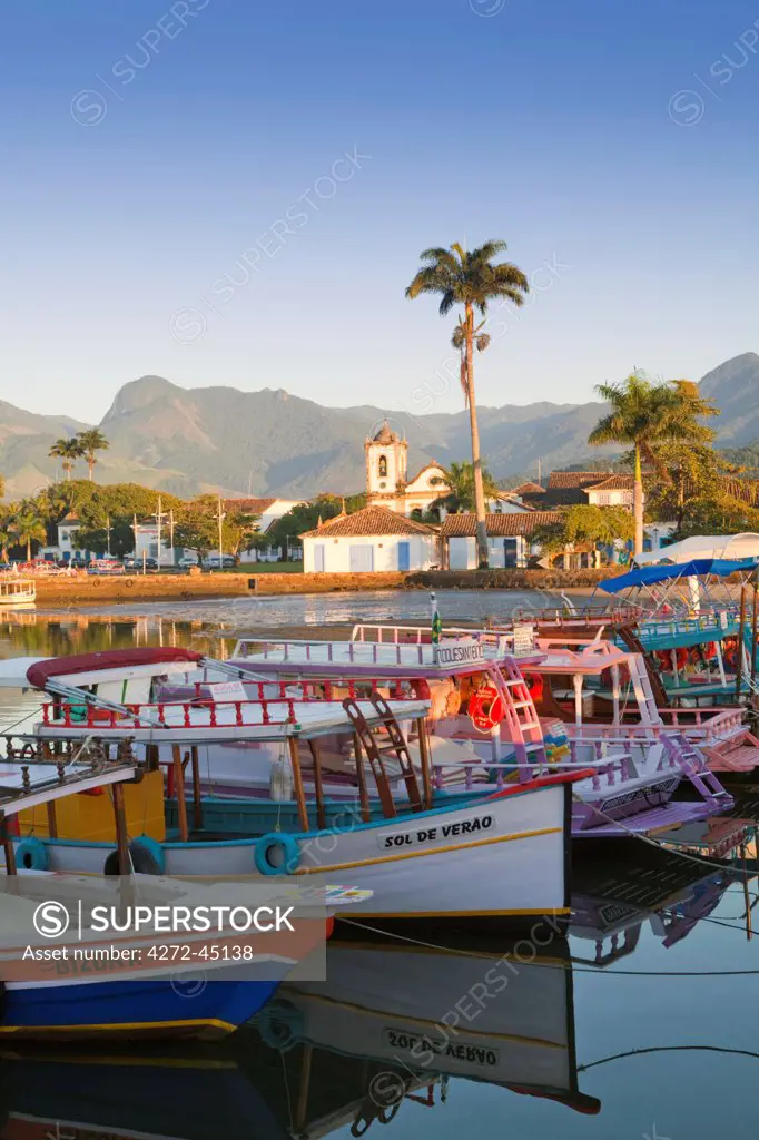 Brazil, Parati, the Portuguese colonial town centre and the church of Saint Rita of Cascia seen from the water with colourful fishing boats in the foreground