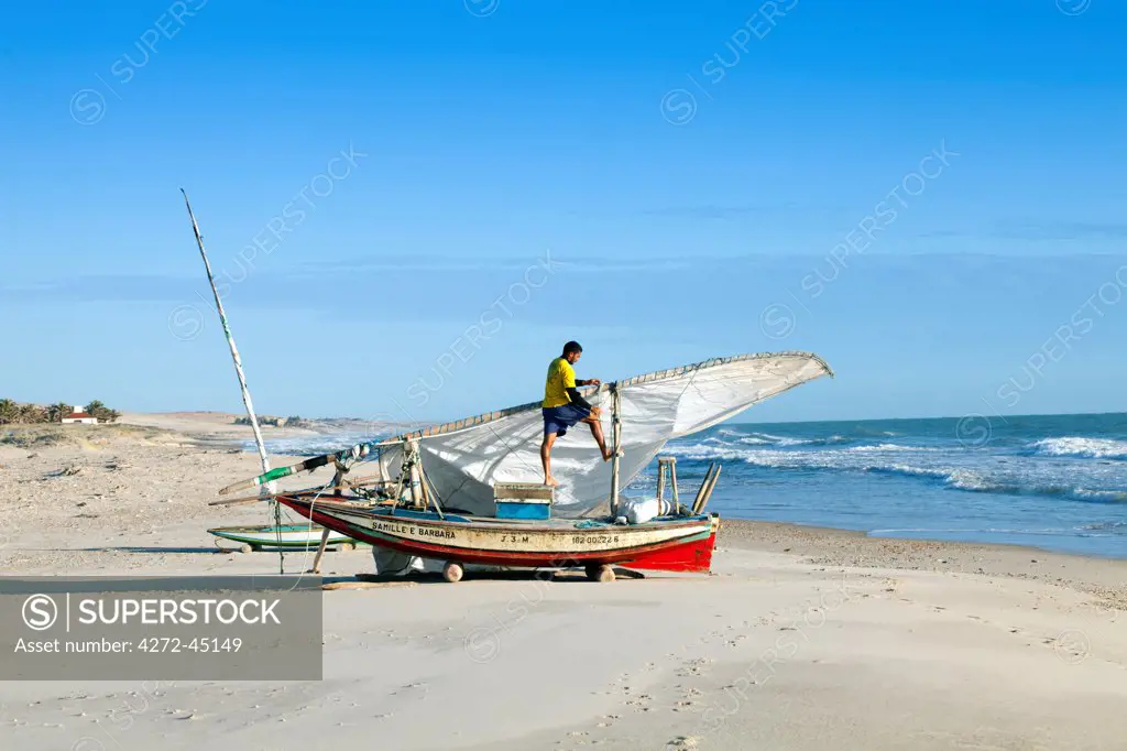 South America, Brazil, Ceara, Fortaleza, a fisherman tending his jangada on the beach in the Prainha do Canto Verde Extractivist Reserve, Reserva Extrativista da Prainha do Canto Verde,. The jangada is said to be the only slightly modified descendant of the boats used by Odysseus