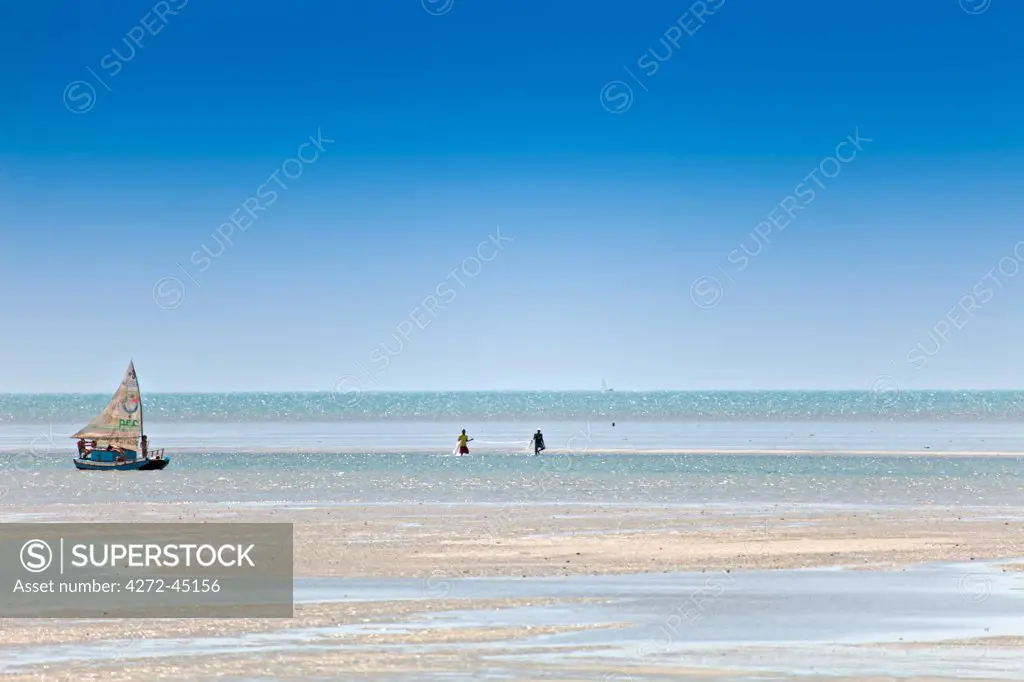 South America, Brazil, Ceara, Fortaleza, fishermen with nets and a jangada walking on the sand flats near the village of Icapui