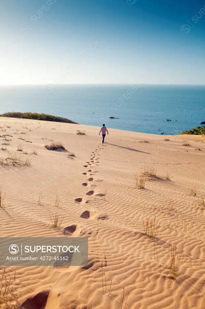 South America, Brazil, Ceara, Morro Branco, a man walks out towards the Atlantic Ocean over the summit of the Morro Branco sand dunes