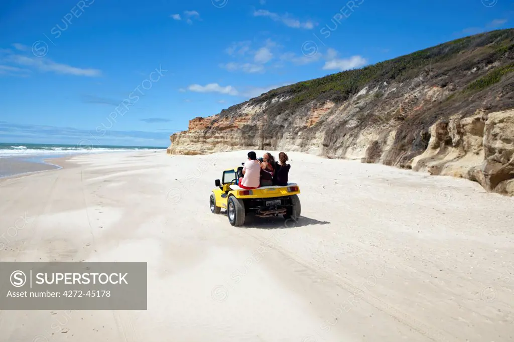 South America, Brazil, Ceara, Morro Branco, tourists riding along a long sandy beach next to the sandstone cliffs near Morro Branco