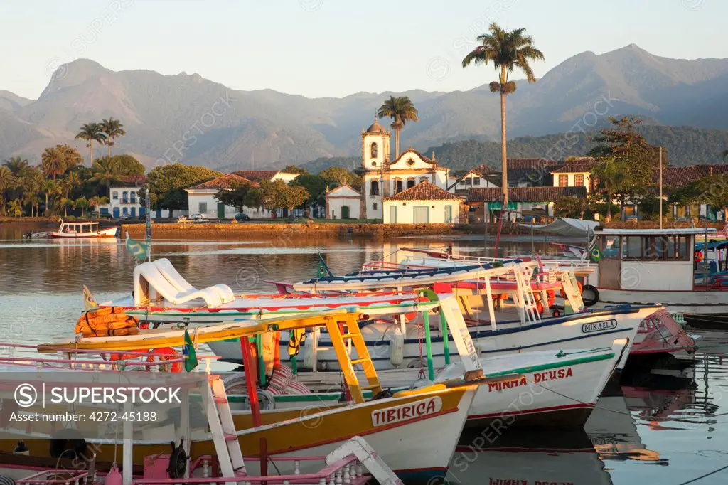 Brazil, Parati, the Portuguese colonial town centre and the church of Saint Rita of Cascia seen from the water with fishing boats on the quay in the foreground