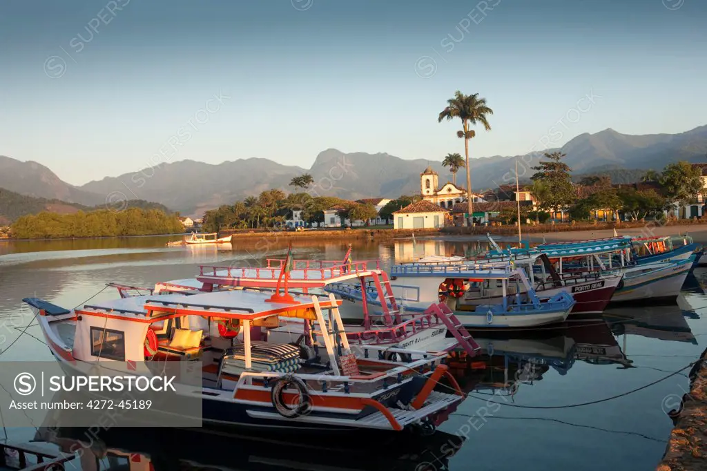 Brazil, Parati, the Portuguese colonial town centre and the church of Saint Rita of Cascia seen from the water with fishing boats on the quay in the foreground
