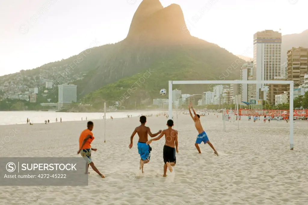 South America, Rio de Janeiro, Rio de Janeiro city, Ipanema, boys playing football on Ipanema beach in front of the Dois Irmaos mountains