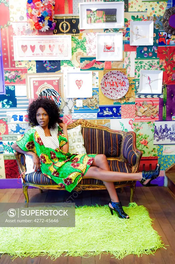 South America, Brazil, Sao Paulo, Jardins, an Afro Brazilian model in designer clothing with a tropical motif sitting on a sofa in the garimpo fuxique boutique in Sao Paulo PR MR