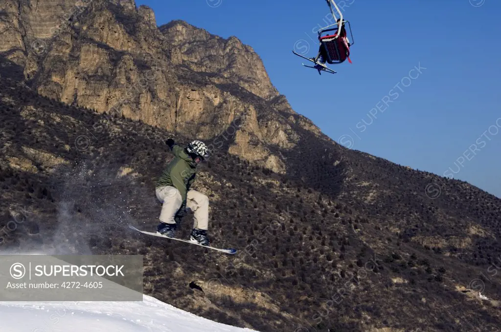 China, Beijing, Shijinglong ski resort. A snowboarder jumping under a ski lift.