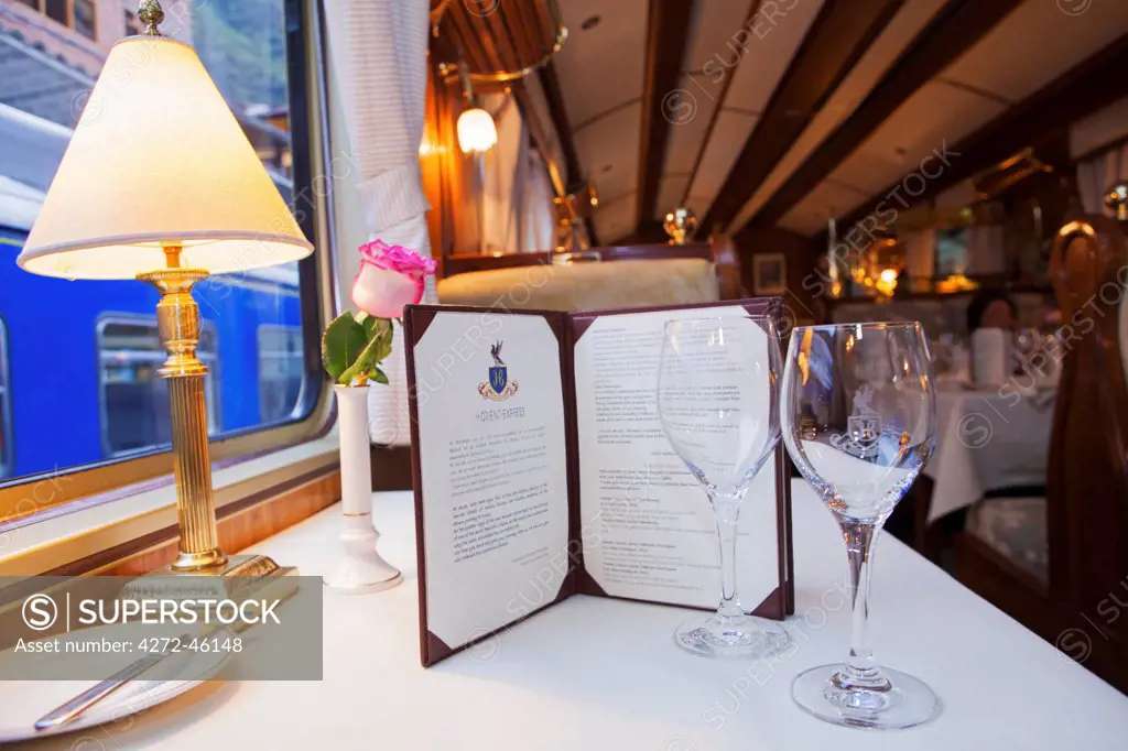 South America, Peru, Cusco, Sacred Valley. A table set for dinner, with branded wine glasses in the dining car of the luxurious Orient Express Hiram Bingham train which runs between Cusco and Machu Picchu via Ollantaytambo