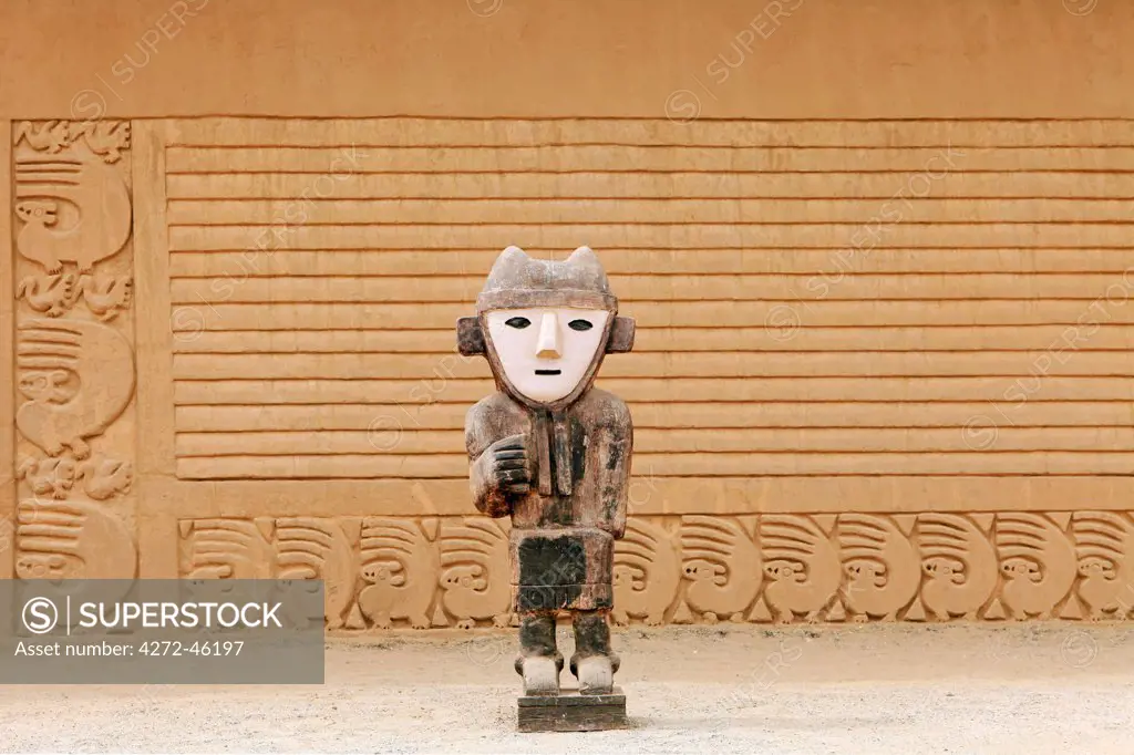 South America, Peru, La Libertad, Trujillo, a wooden statue in front of a carved adobe wall in the Chimu city of Chan Chan a World Heritage site