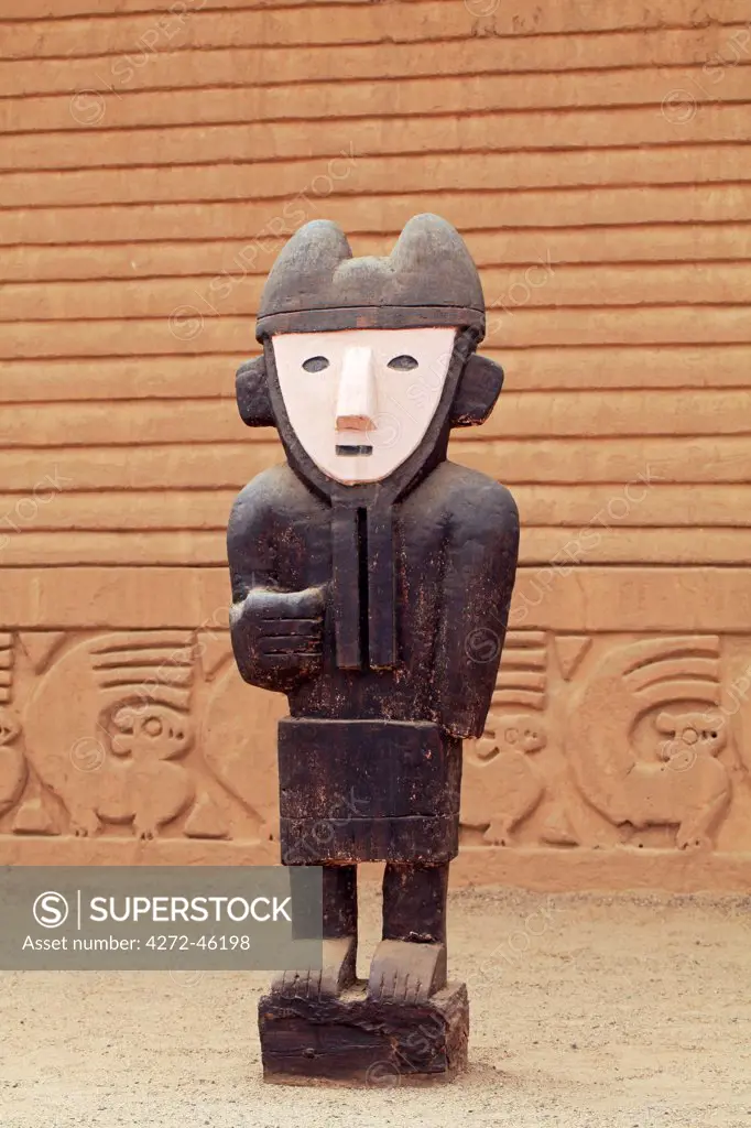 South America, Peru, La Libertad, Trujillo, a wooden statue in front of a carved adobe wall in the Chimu city of Chan Chan, a World Heritage site