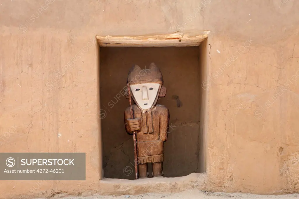 South America, Peru, La Libertad, Trujillo, a wooden statue in front of a carved adobe wall in the Chimu city of Chan Chan a World Heritage site