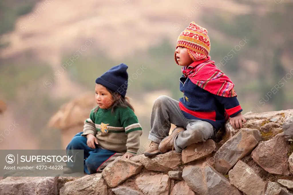 South America, Peru, Cusco, Sacred Valley, Pisac. Quechua children, one wearing a chullo at the Pisac ruins in the hills above the Urubamba valley. The first chullo that a child receives is traditionally knitted by his father.