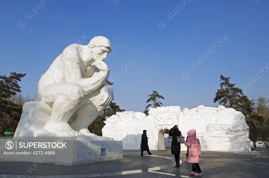 China, Northeast China, Heilongjiang Province, Harbin City. Snow and Ice Sculpture Festival at Sun Island Park. Visitors standing beneath a thinking man sculpture.