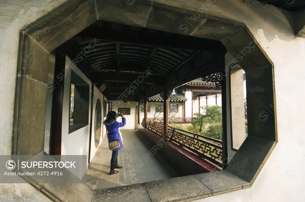 China, Jiangsu Province, Suzhou City. Garden of the Master of the Nets laid out in the 12th century, a view through a window of a girl photographing the garden, World Heritage listed by UNESCO