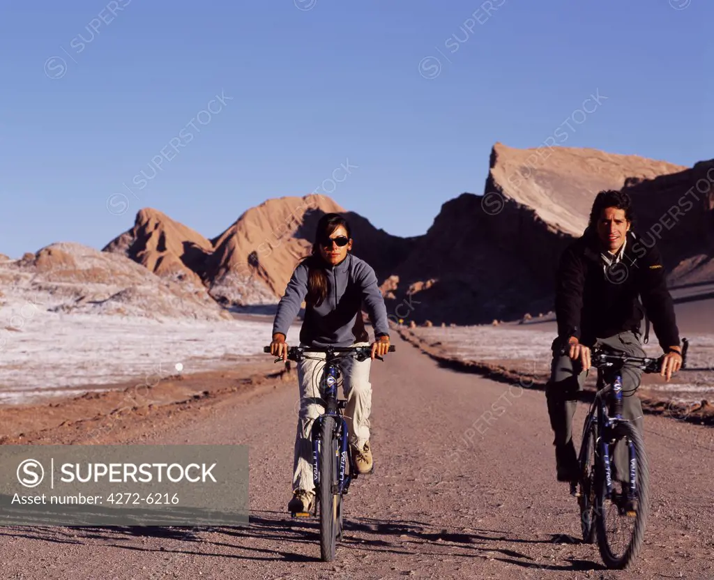 Tourists mountain biking in the striking landscape of Moon Valley near to San Pedro de Atacama in the Atacama Desert which is characterised by wind-eroded hills and a mineral crusted valley floor.