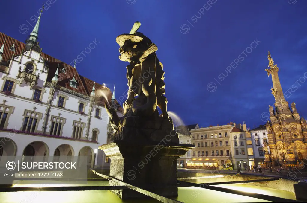 Czech Republic, Moravia, Olomouc, Fountain In Front Of Town Hall In Upper Square (Horni Nam) At Dusk With Holy Trinity Column In Background