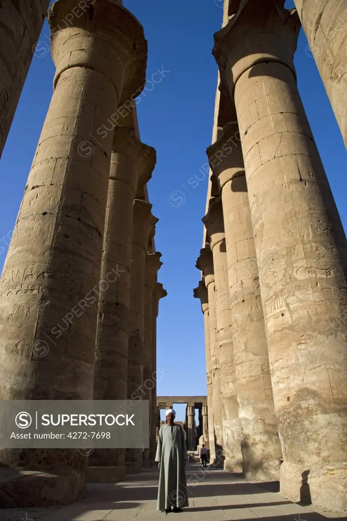 A guardian stands beneath the giant columns of the processional collonade built by Amenophis III at Luxor Temple, Egypt.