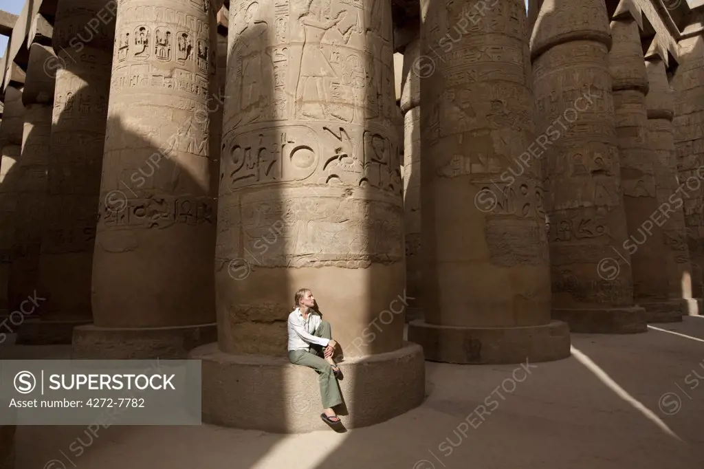 Egypt, Karnak. A tourist sits at the base of a massive stone column in the Great Hypostyle Hall. (MR)