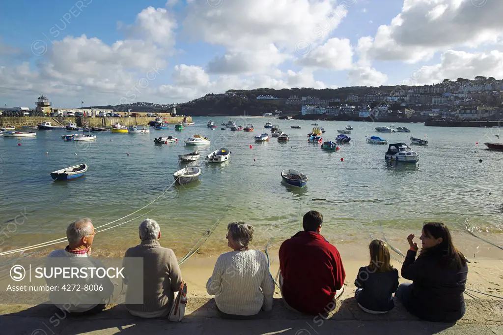 A group of tourists chat and eat ice creams while sitting on the quayside in St Ives, Cornwall.