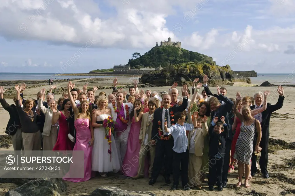 A wedding party pose for a photograph in front of St Michaels Mount,  Marazion, Cornwall, England