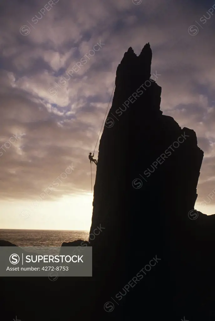 England, Devon, Lundy Island. Climber abseiling the Needle at dusk on the Island of Lundy. Lundy Island lies in the Bristol Channel, about 11 miles off the coast of North Devon. Three miles long and half a mile wide, this granite outcrop rises 400 feet above sea level and is a place of outstanding natural beauty, with tremendous views of England, Wales and the Atlantic.