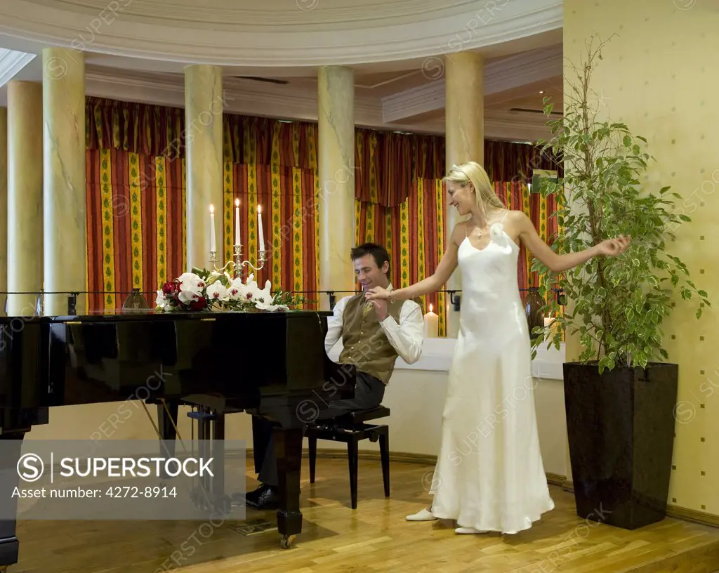 England, Northern Ireland, Londonderry. Bride dancing to the music played by the Groom on the piano during their wedding day at the Everglades Hotel. (MR).