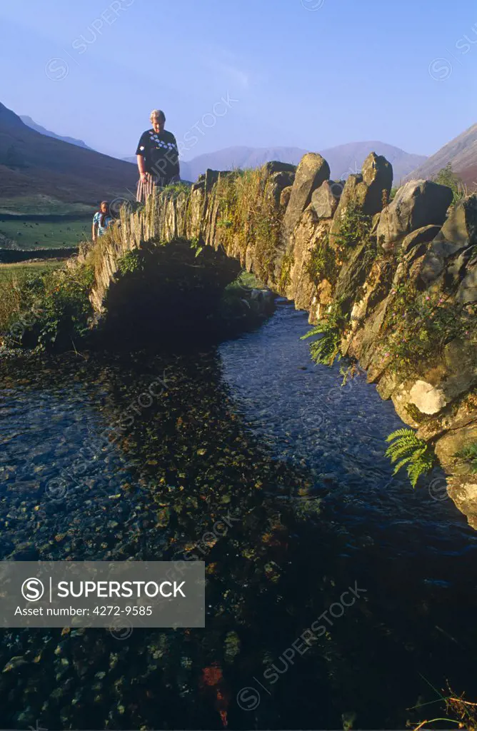 Eskdale, Cumbria, Walkers crossiing a tradition stone bridge.