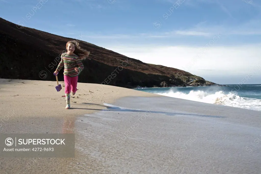 England, Cornwall. Young girl running across the sands at Portheras Cove near Pendeen on the Penwith Peninsula. (MR)