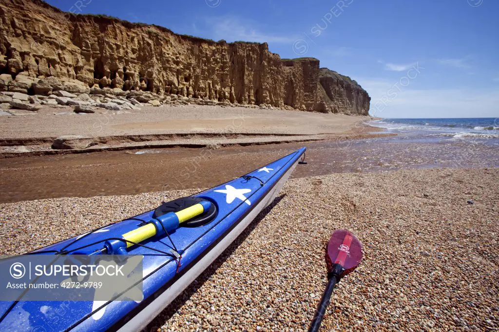 England, Dorset, Bridport.  A sea kayak rests in the shadow of the famous cliffs of the UNESCO World Heritage Jurassic Coast.