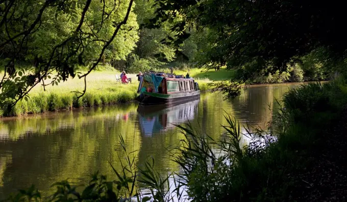 UK, Berkshire. A family have a picnic on the banks of a canal, beside their canal boat.