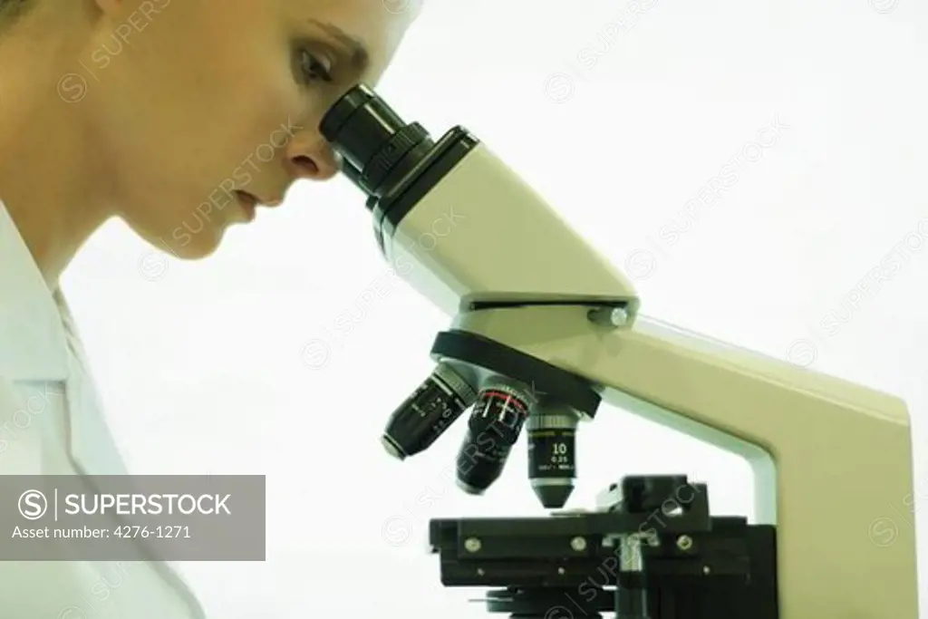 Female scientist looking through microscope, side view