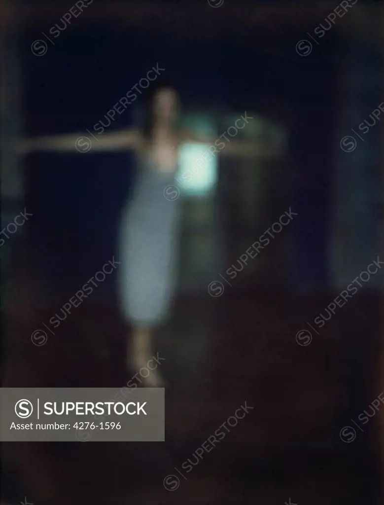 Female figure with arms out in dark room, defocused